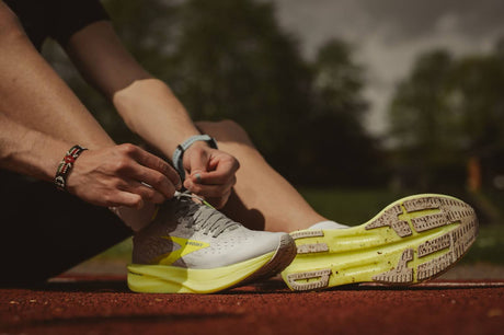  A man is seated on the ground, fastening his athletic and running shoes.